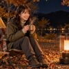 秋の夜のキャンプ場で、ストーブのそばで温かい飲み物を手に暖まっている