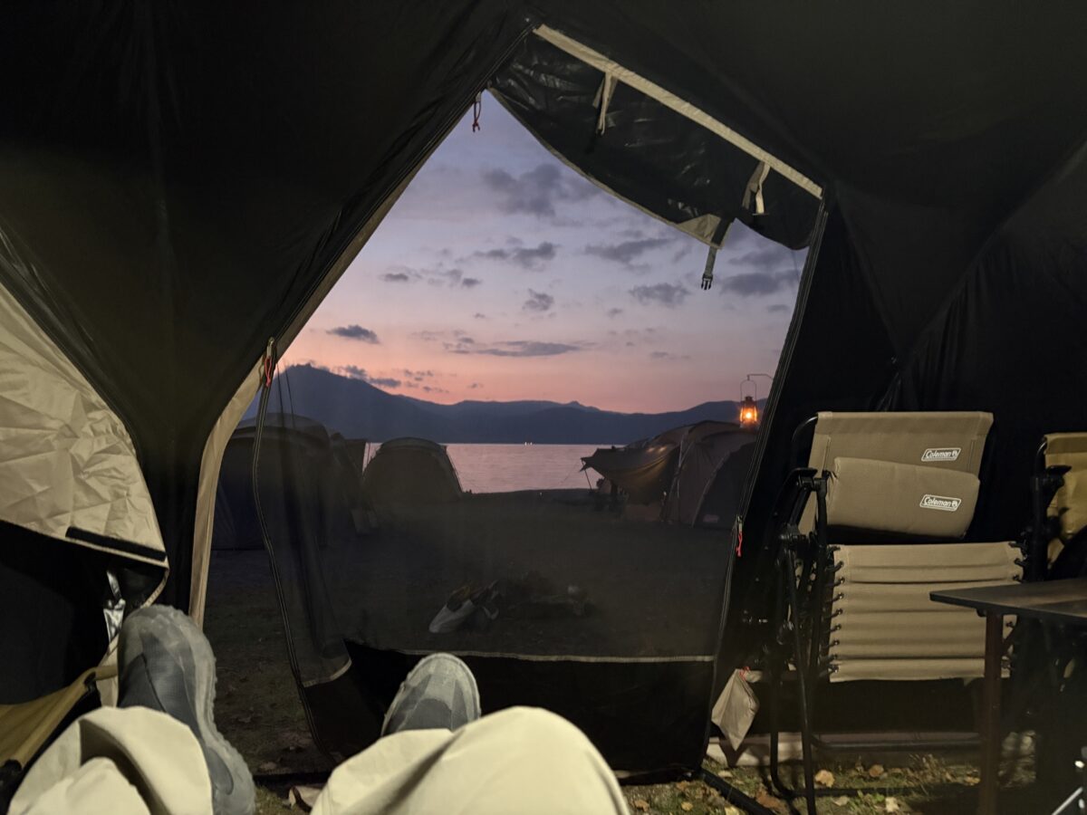 テントの入口から眺める秋の湖の夕焼け